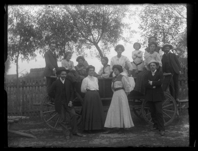 Portret zbiorowy przy wozie w ogrodzie. Przed wozem w jasniej sukni stoi Dorota Janusz. Po prawej stronie na wozie Maria Janusz (siedzi najwyżej). Część osób to rodzina brata Edwarda Janusza