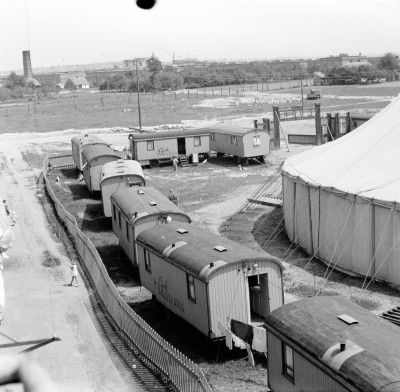 Cyrk Warszawa na placu zabaw przy górce obok Osiedlowych Plantów przy ul. Bolesława Krzywoustego. Na drugim planie domy i ogrody przy ul. Piastów, dalej komin kotłowni i bloki przy ul. Stanisława Staszica, a w oddali wznoszone wieżowce przy ul. Teofila Lenartowicza
