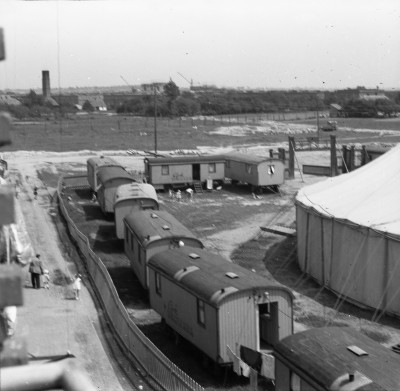 Cyrk Warszawa na placu zabaw przy górce obok Osiedlowych Plantów przy ul. Bolesława Krzywoustego. Na drugim planie domy i ogrody przy ul. Piastów, dalej komin kotłowni i bloki przy ul. Stanisława Staszica. W tle wznoszone wieżowce przy ul. Teofila Lenartowicza