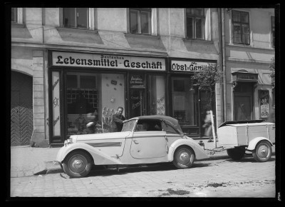 Mężczyzna przy samochodzie z przyczepą przed witryną sklepu z artykułami spożywczymi w Wiedniu