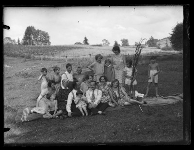 Grupa ludzi w plenerze. Po prawej stoją: Krystyna Urban z mamą Marią i kuzynami Ireną i Marianem Elgas (klęczy czwarty od lewej), na dole po prawej siedzi Dorota Elgas